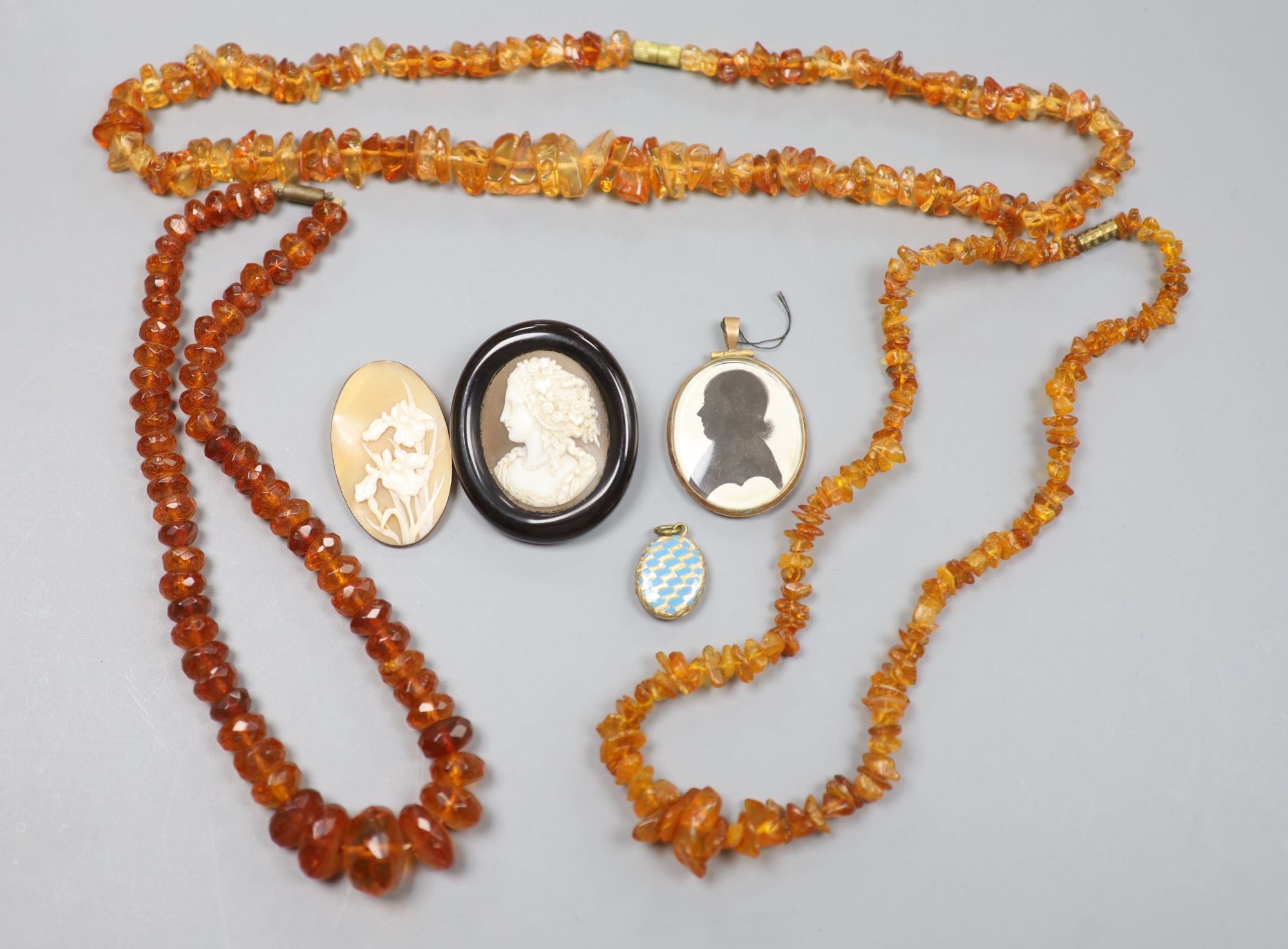 A 9k mounted cameo shell brooch, 46mm, a silhouette pendant, brooch, locket and two amber necklaces.